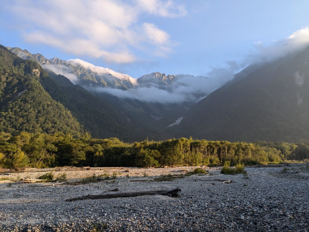 A misty morning view of the rugged Hotaka Mountain range in Kamikochi, Japan, showcasing a rugged valley and low clouds. The image captures the serene, undisturbed atmosphere essential for mindful travel, encouraging travelers to stop and savor the natural beauty.