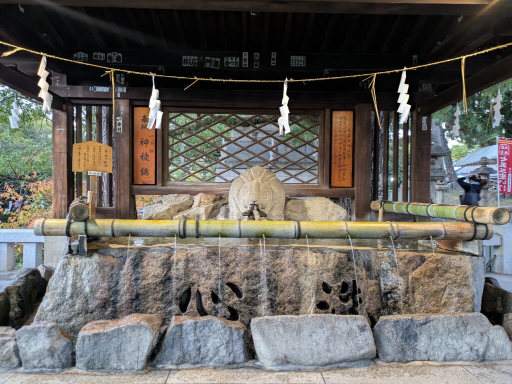 Close-up of a stone Temizuya water basin at a Japanese shrine, with bamboo and wooden ladles resting on a rack over clear flowing water. Using this respectfully is a key part of Japanese etiquette and temple respect.