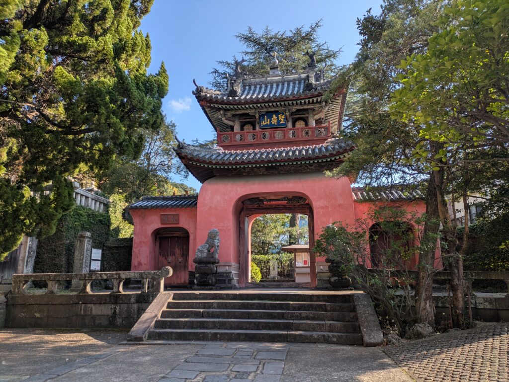 The iconic red Ryugumon entrance gate of Sofuku-ji Temple in Nagasaki, a National Treasure of Japan, featuring an ornate two-story roof and traditional Chinese-influenced architecture.