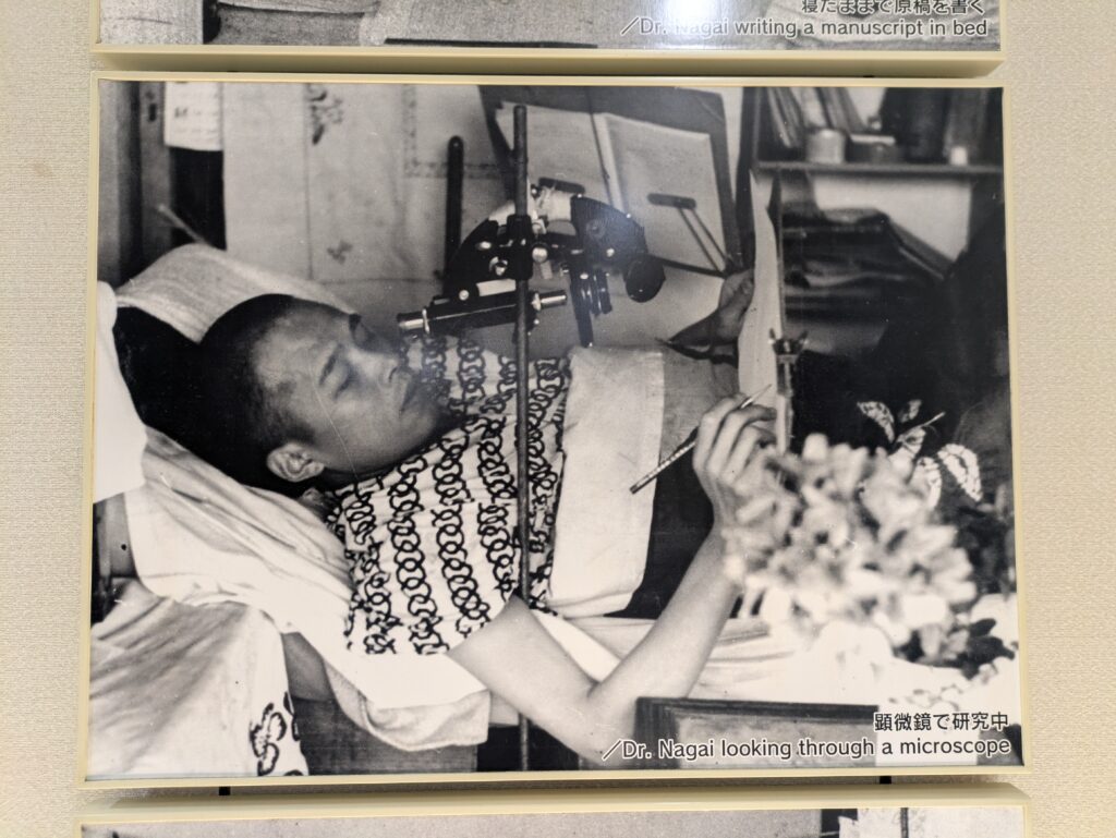 A black and white portrait photo of Dr. Takashi Nagai, a Japanese radiologist and atomic bomb survivor, wearing traditional patterned clothing, propped up in his sick bed while holding a small object.
