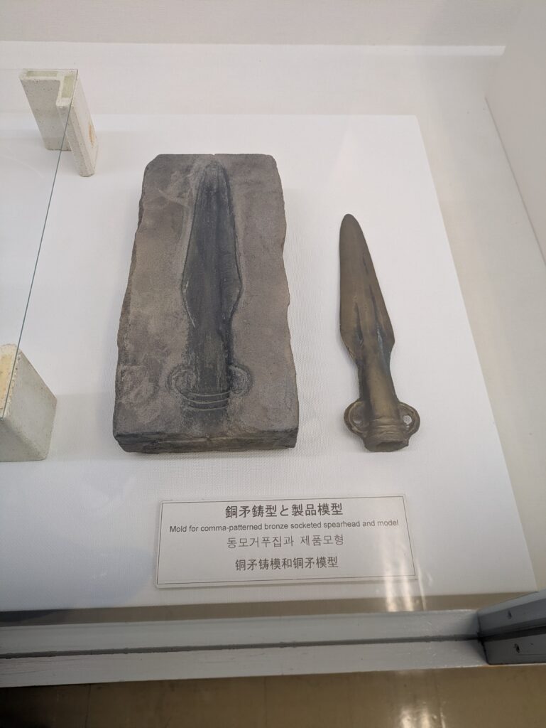 Ancient bronze spearhead and stone mold on display in a glass museum case.