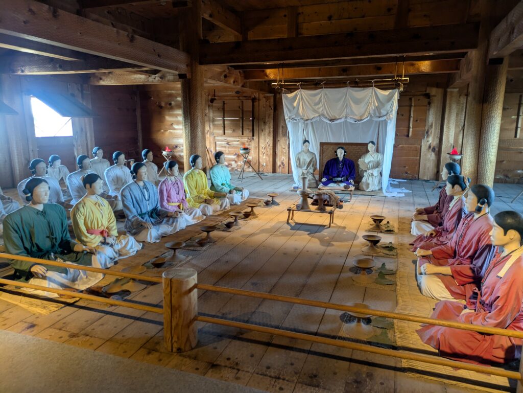 Interior of the reconstructed Great Hall at Yoshinogari, featuring a ceremonial assembly of life-sized mannequins in ancient Yayoi period clothing.