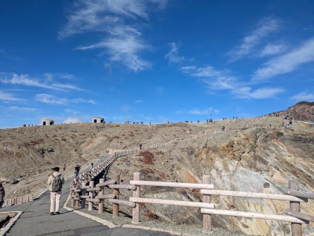 Walking path with wooden fences leading up to the active volcano rim of Mt. Aso, Kumamoto Japan.