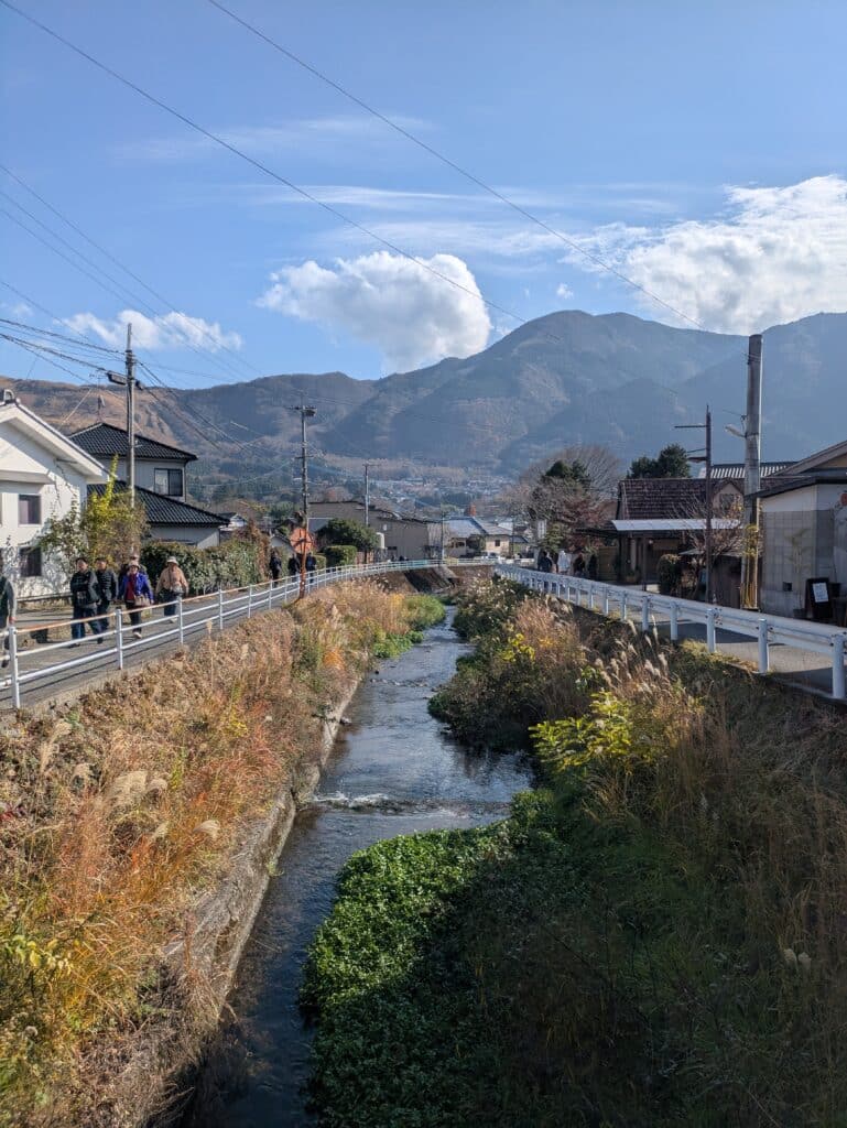 Scenic view of a small river flowing through Yufuin village with a large mountain peak in the background under a blue sky.