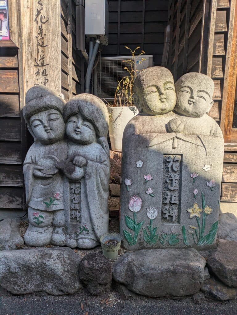 Two pairs of small, smiling stone Jizo statues decorated with painted flowers in Yufuin, Japan.