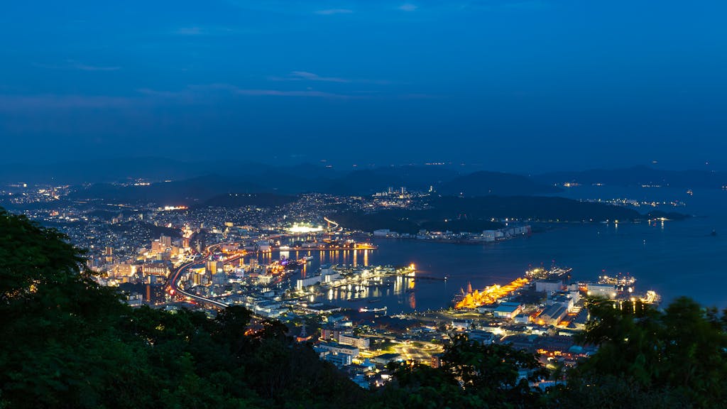 Dazzling evening view of Nagasaki harbor with illuminated cityscape and vibrant shipping terminals.
