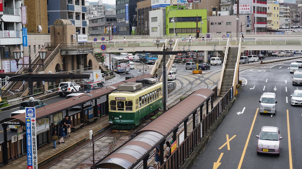 Urban scene in Nagasaki City featuring a tram and bustling street traffic with a pedestrian overpass.