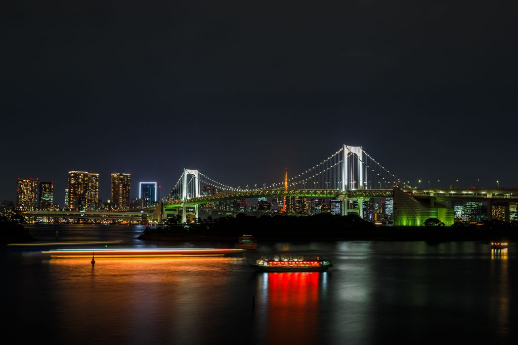 Night view of Rainbow Bridge in Tokyo with city skyline and reflections on water.
