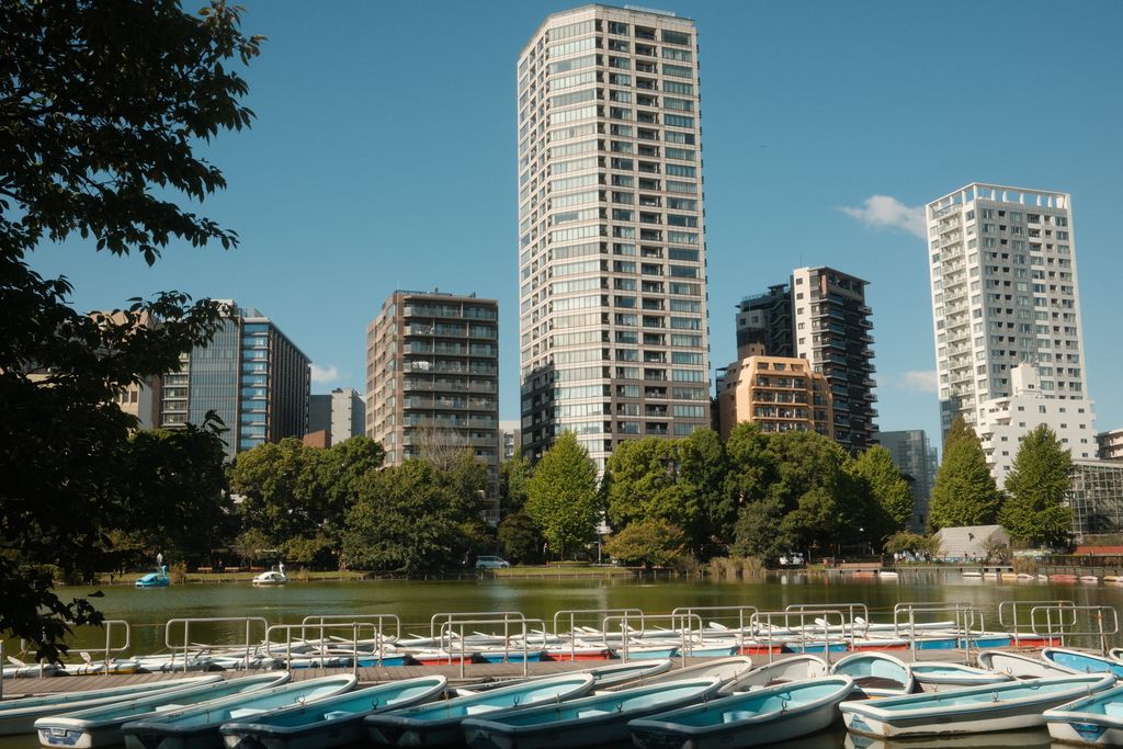 A serene view of boats on Shinobazu Pond against Tokyo's urban skyline in Taito City.